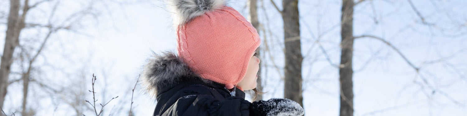 un bébé fille qui regarde le ciel avec une tuque rose et un pompom dans la foret