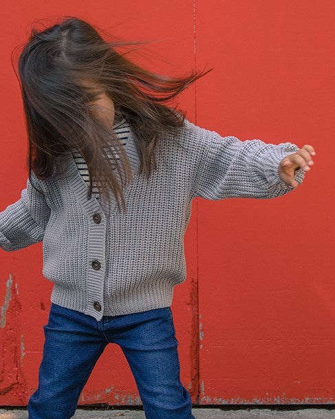 une jeune fille qui porte un tricot gris avec des bouton de la marque Romy et Aksel 